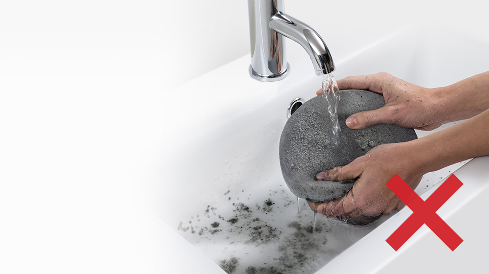A dirty, dust-clogged filter being washed in the sink.